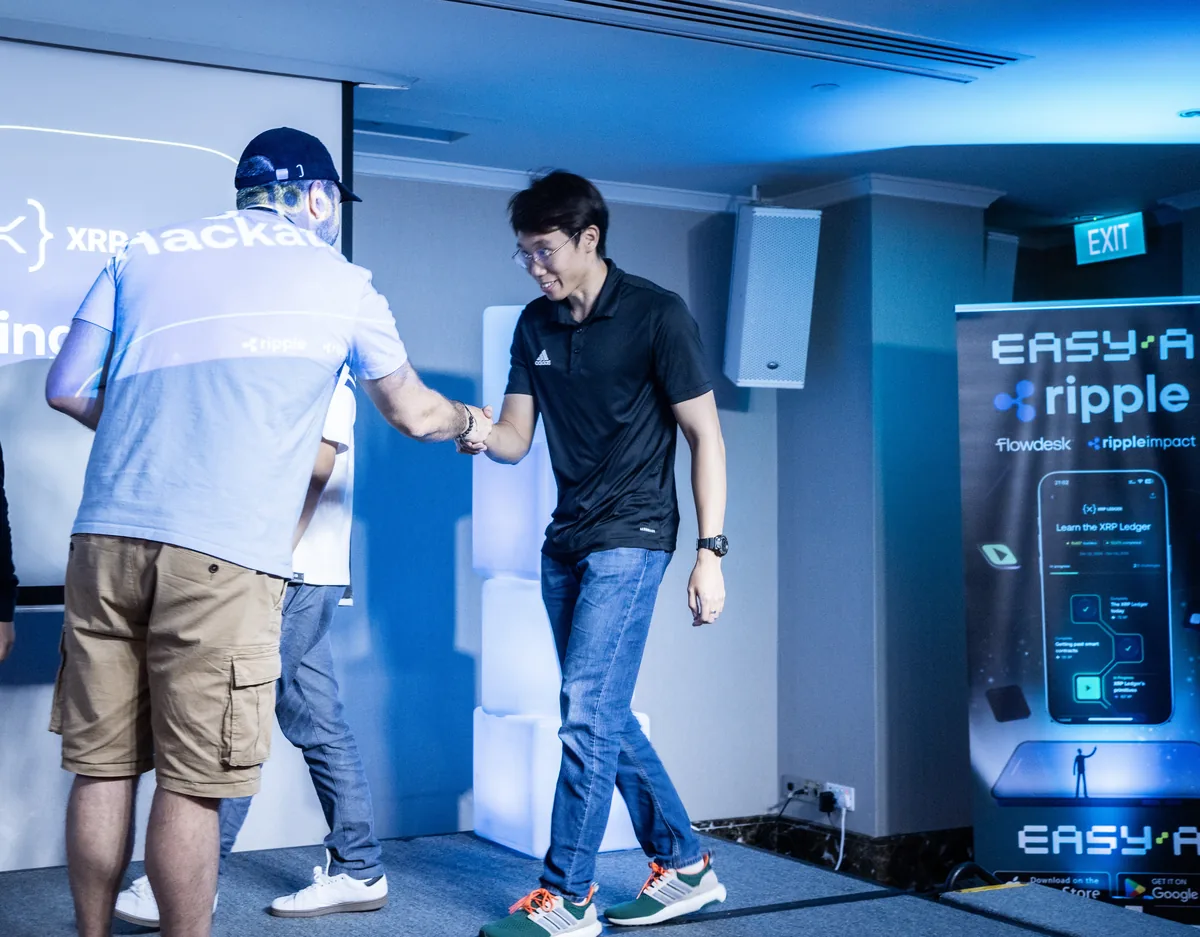 A handshake on stage at the EasyA x Ripple hackathon in Singapore, by the EasyA and Ripple banner